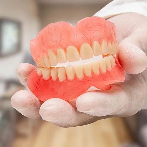 gloved hand holding a pair of dentures