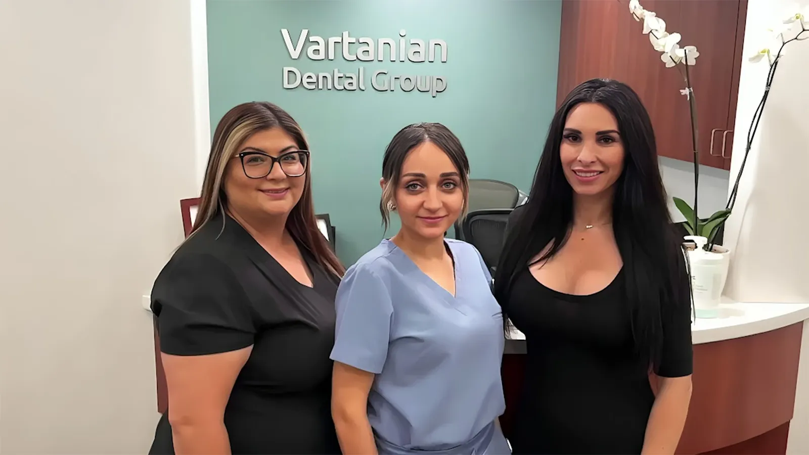 Three women, dental assistants, posing at the front desk.