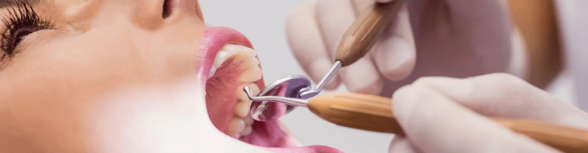 Gloved hands using dental tools in woman's mouth.