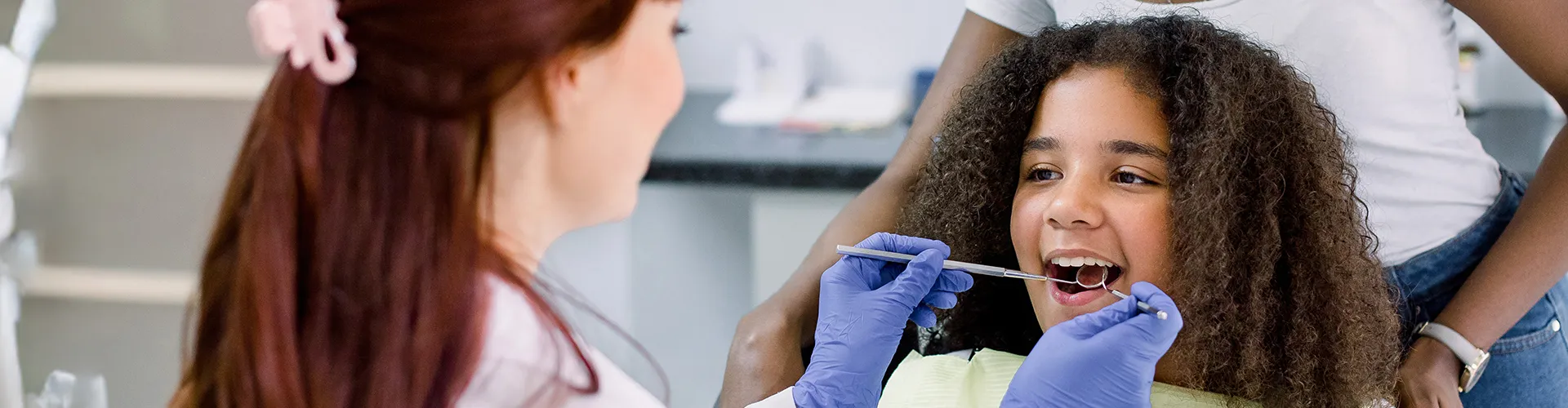 Dentist's gloved hands using dental tools in girl's mouth.