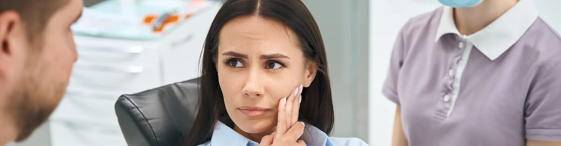 woman holding her cheek in pain in front of dentist