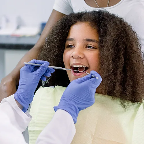 Dentist's gloved hands using dental tools in girl's mouth.